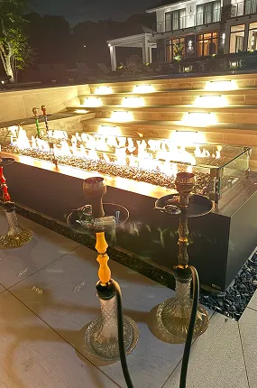 Three hookahs standing by a gas fire pit on a lit terrace at night during a private event
